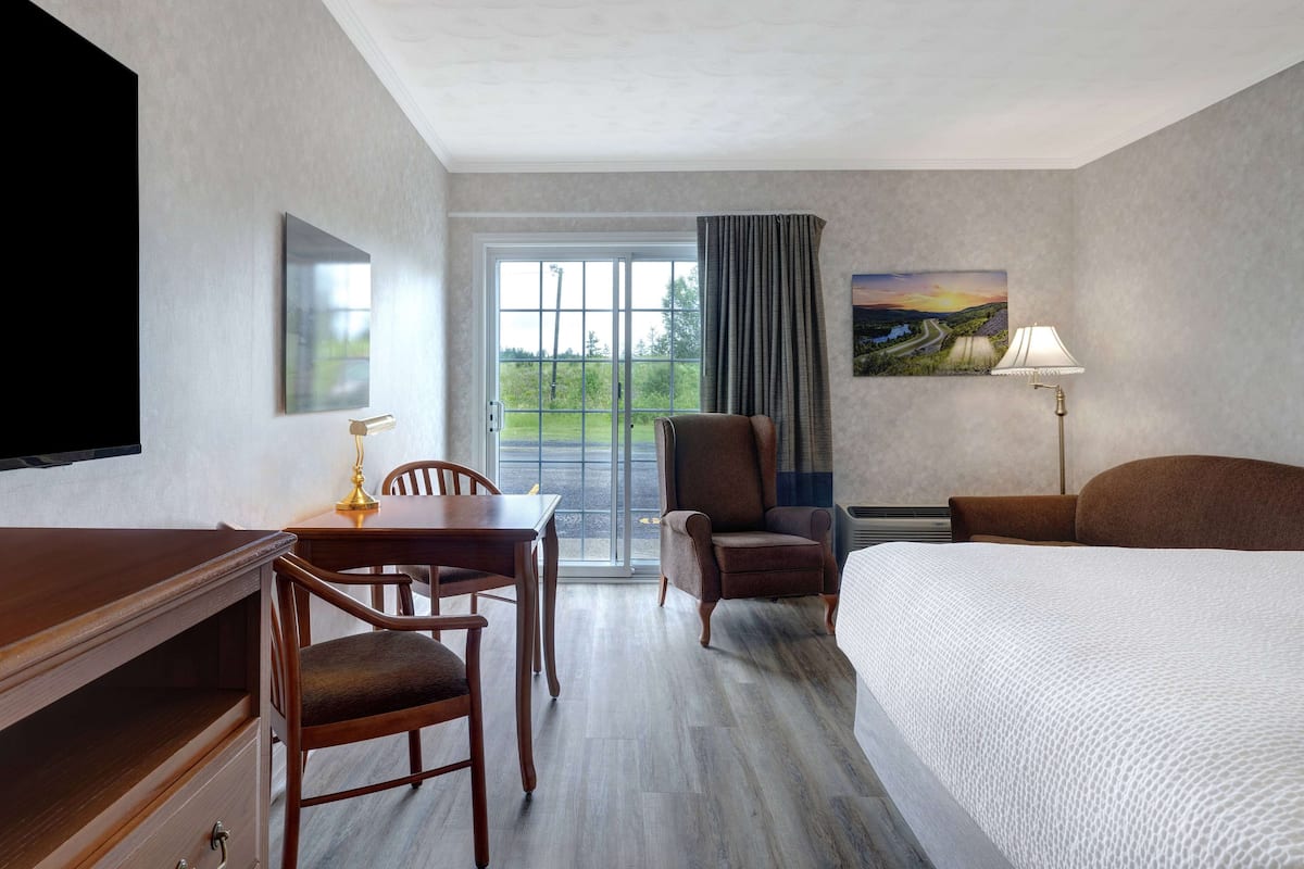 Habitación de hotel con cama, escritorio y silla, televisor, un cuadro y ventana con cortinas.