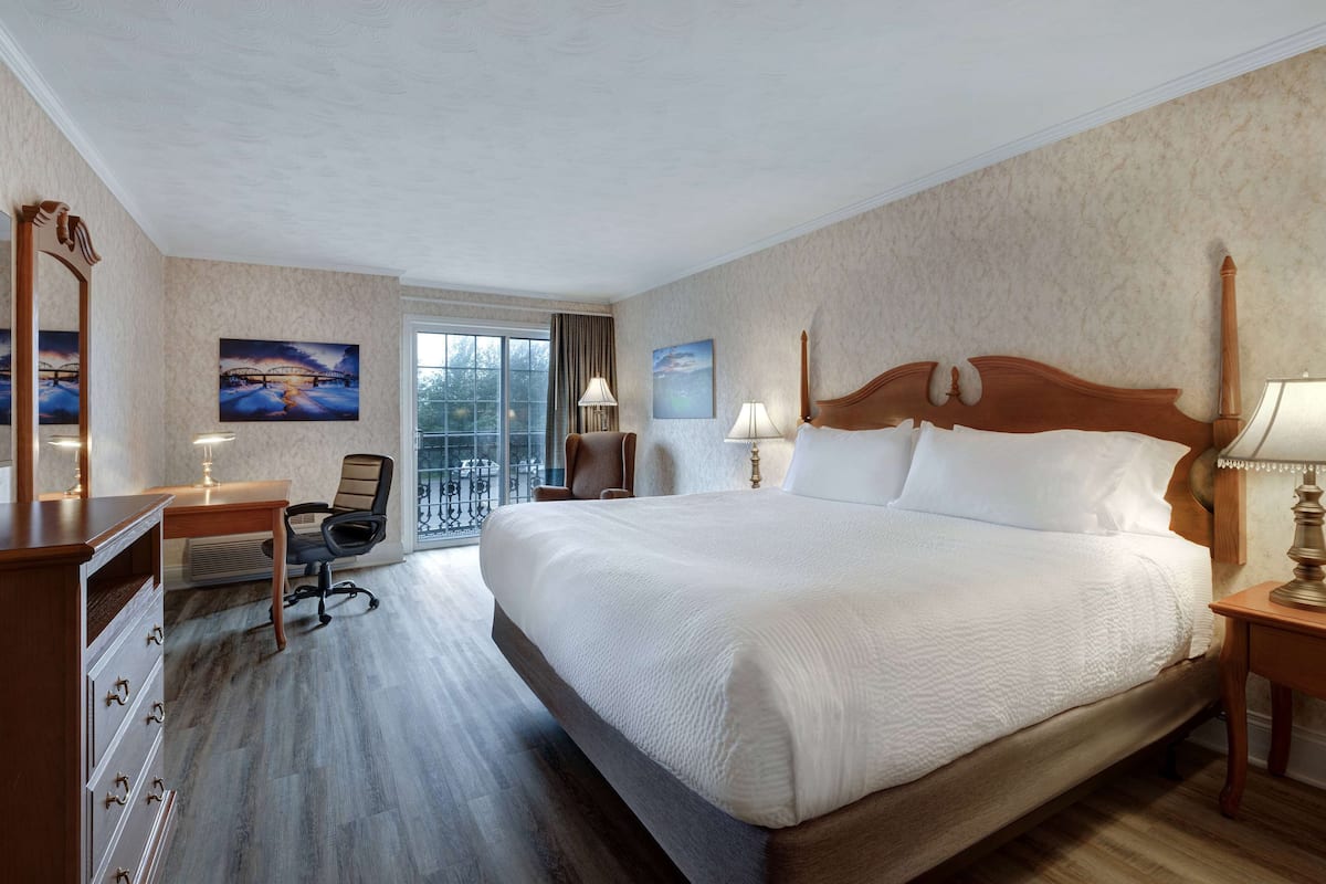 Habitación de hotel con una cama grande, un escritorio con silla, un aparador y un ventanal con vistas.