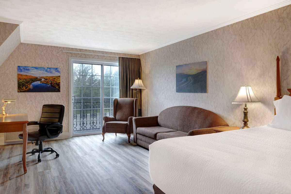 Habitación de hotel con una cama grande, un escritorio con lámpara, una silla y dos cuadros en las paredes.