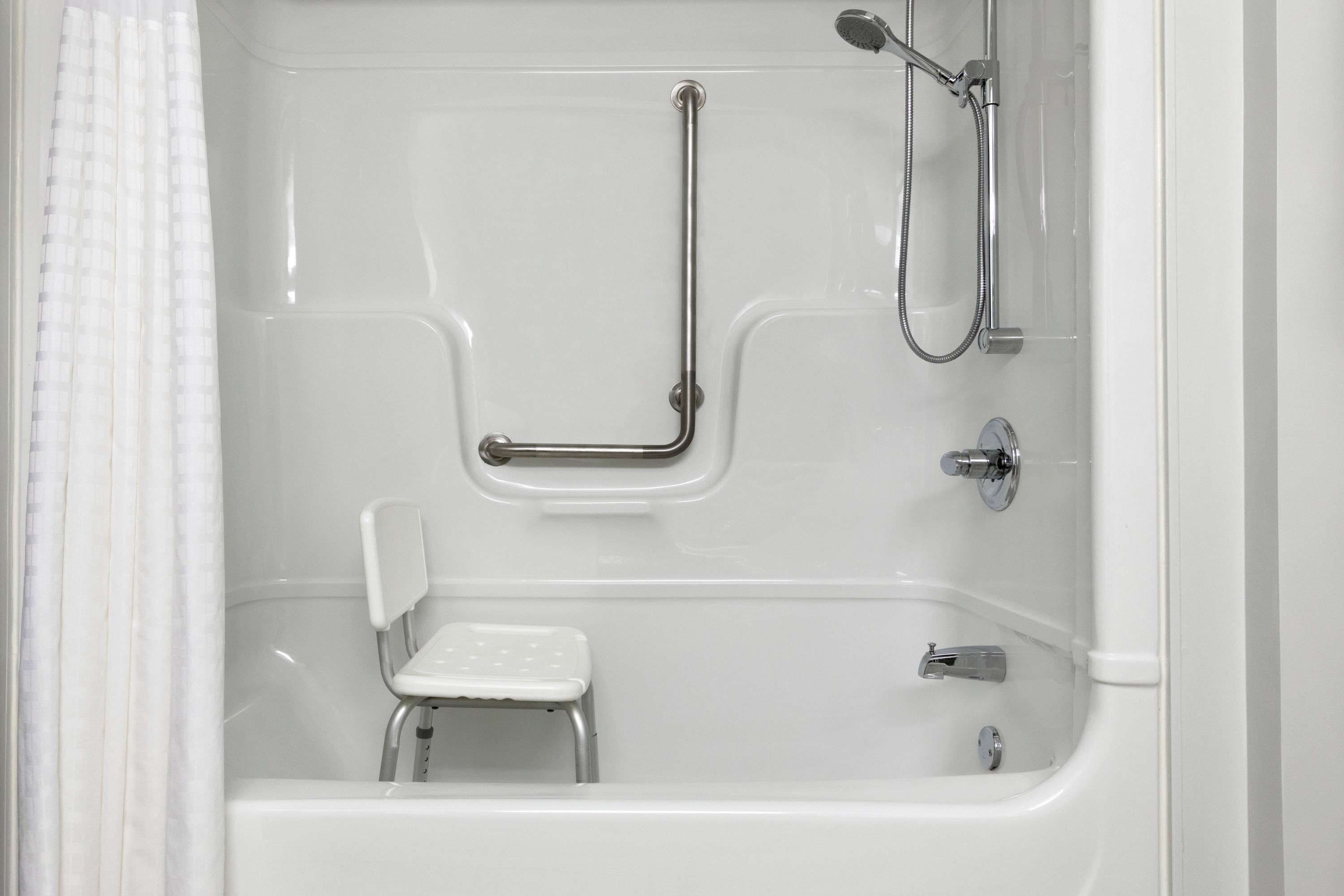 A white bathtub with a built-in seat, grab bars, and a handheld showerhead.