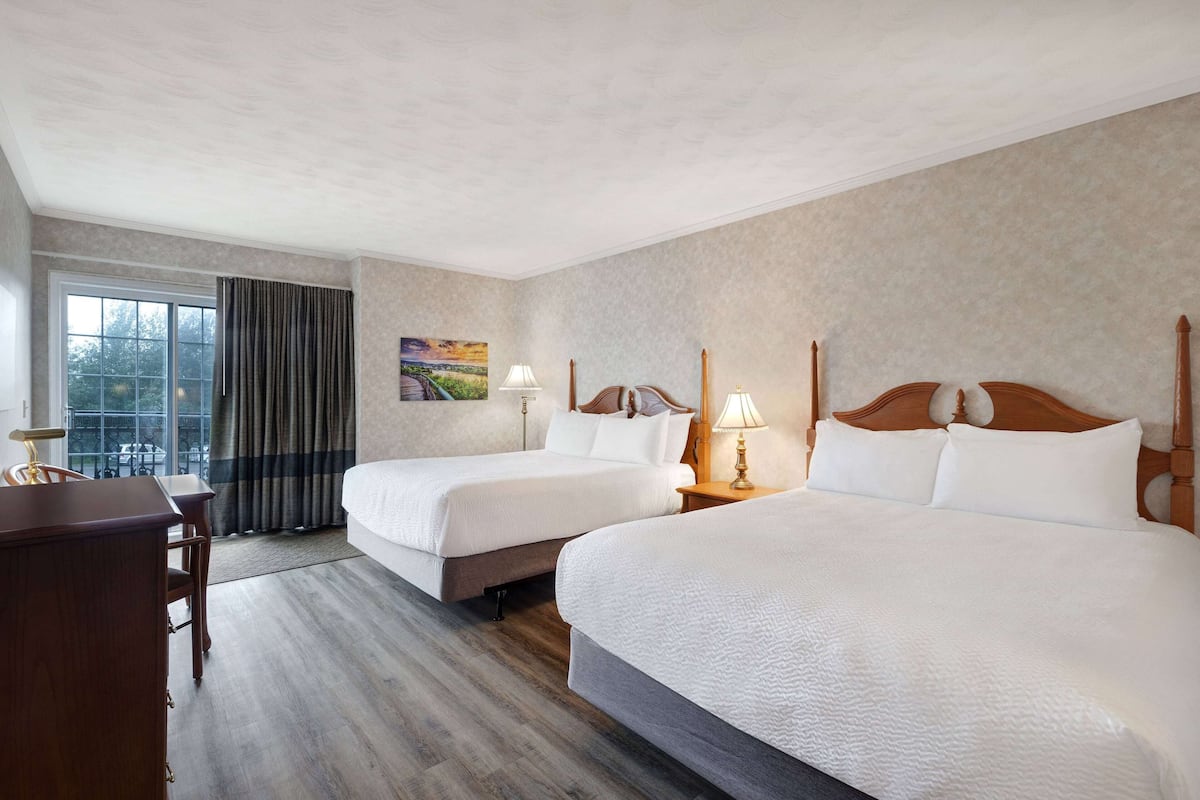 Habitación de hotel con dos camas, un escritorio y una ventana con cortinas.