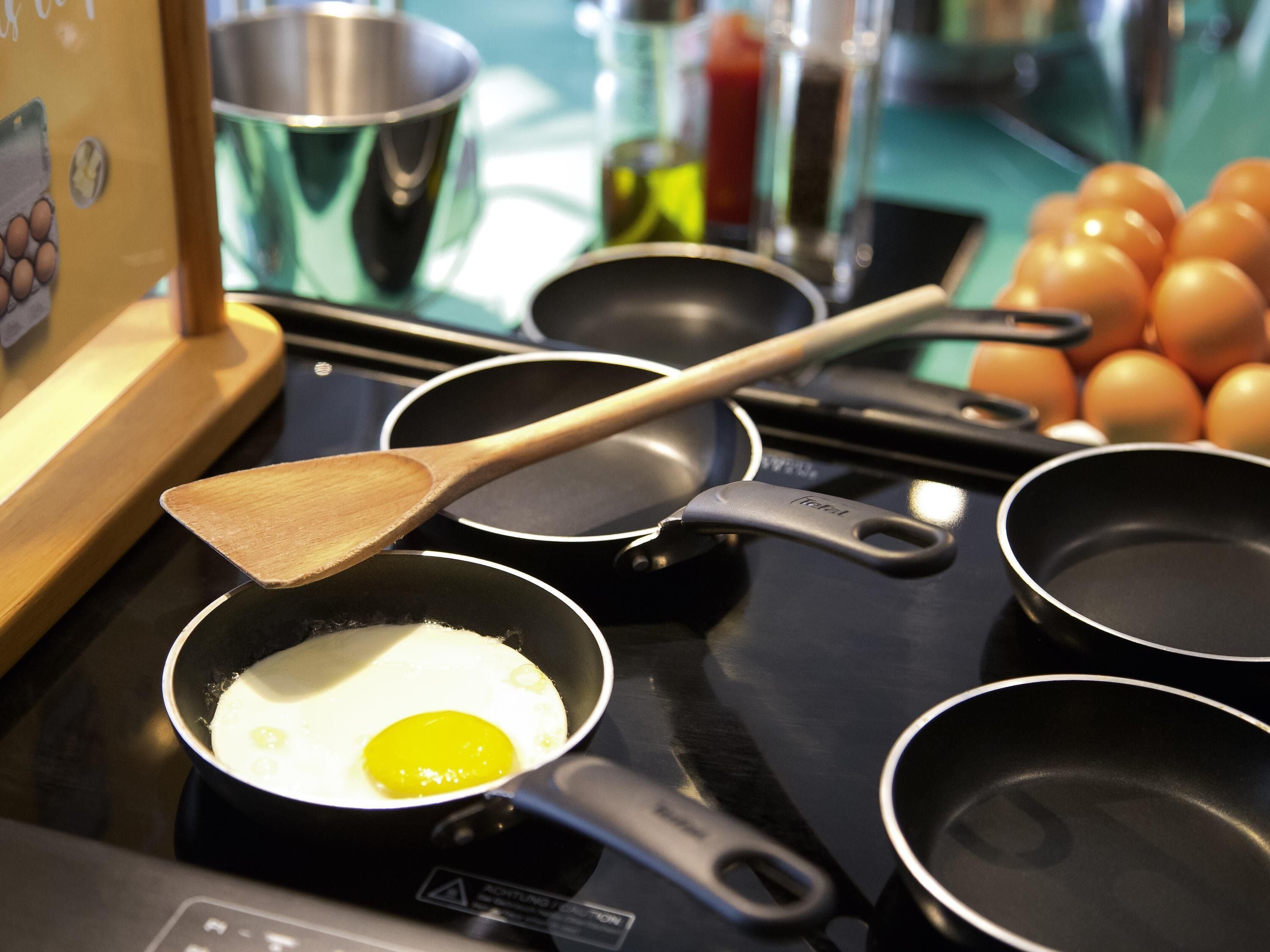 A kitchen with a frying pan on an induction cooktop, a wooden spatula, and a pot.