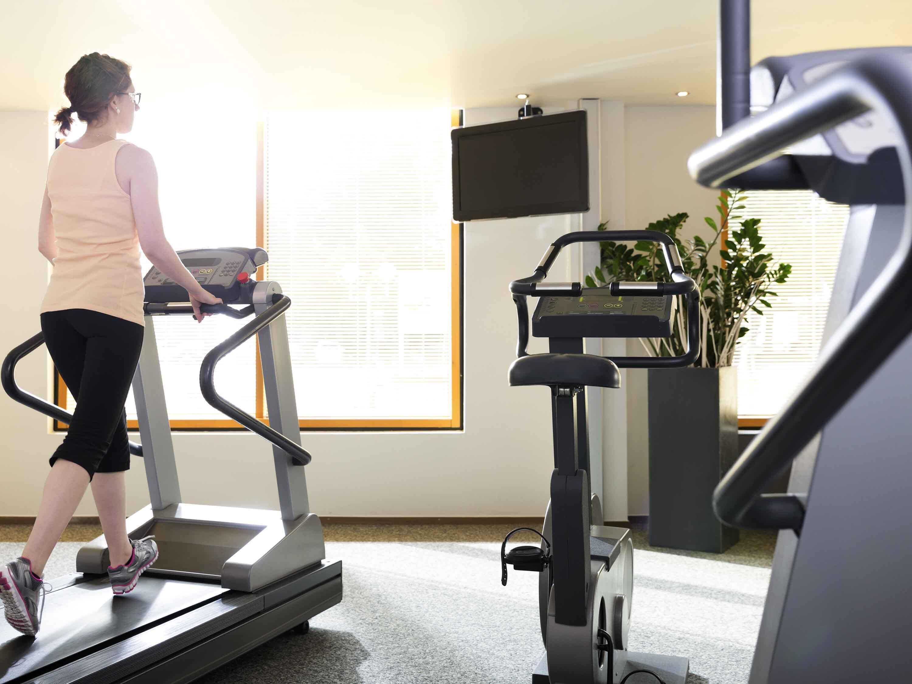 A person using a treadmill in a room with a large window, a television, and a plant.