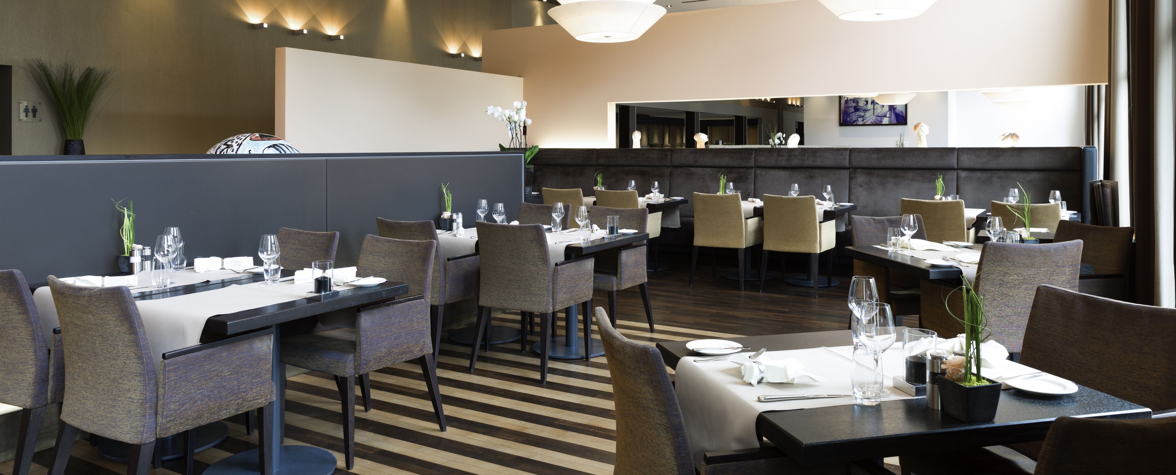 Un restaurante moderno con una distribución limpia y ordenada, que cuenta con varias mesas y sillas, piso a rayas y una paleta de colores neutros.
