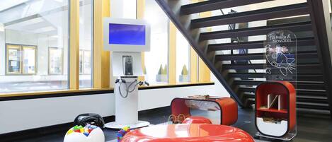 A modern interior with a large window, a digital screen, a red seating area, and a Family & Novotel sign.