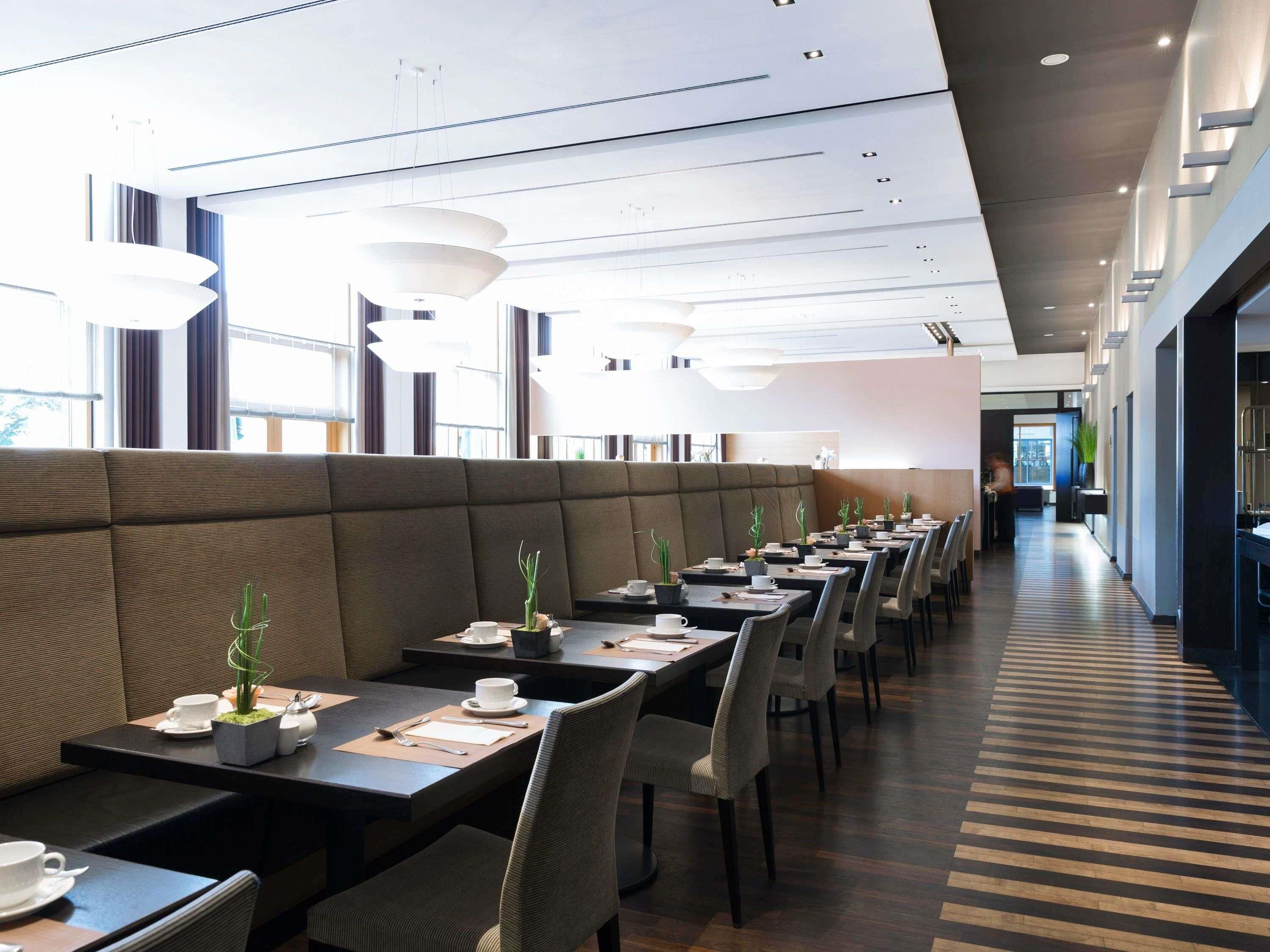 A modern restaurant with long communal tables, cushioned booths, and pendant lighting.