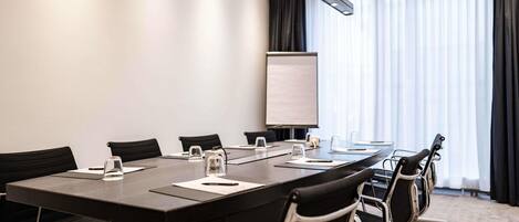 A conference room with a long table, black chairs, a whiteboard, and a window with curtains.