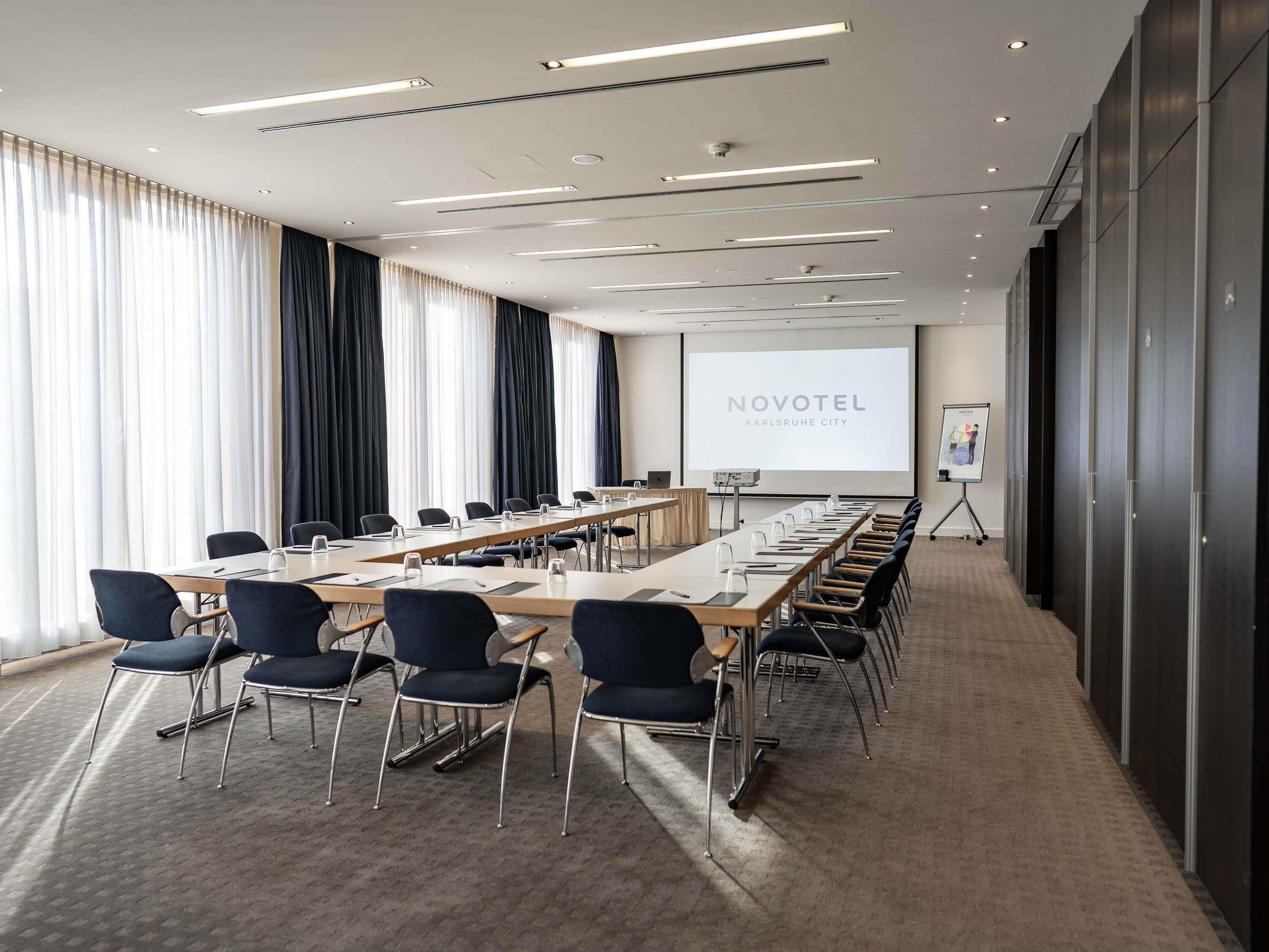 A conference room with a long table, chairs, a projector screen, and a presentation board.