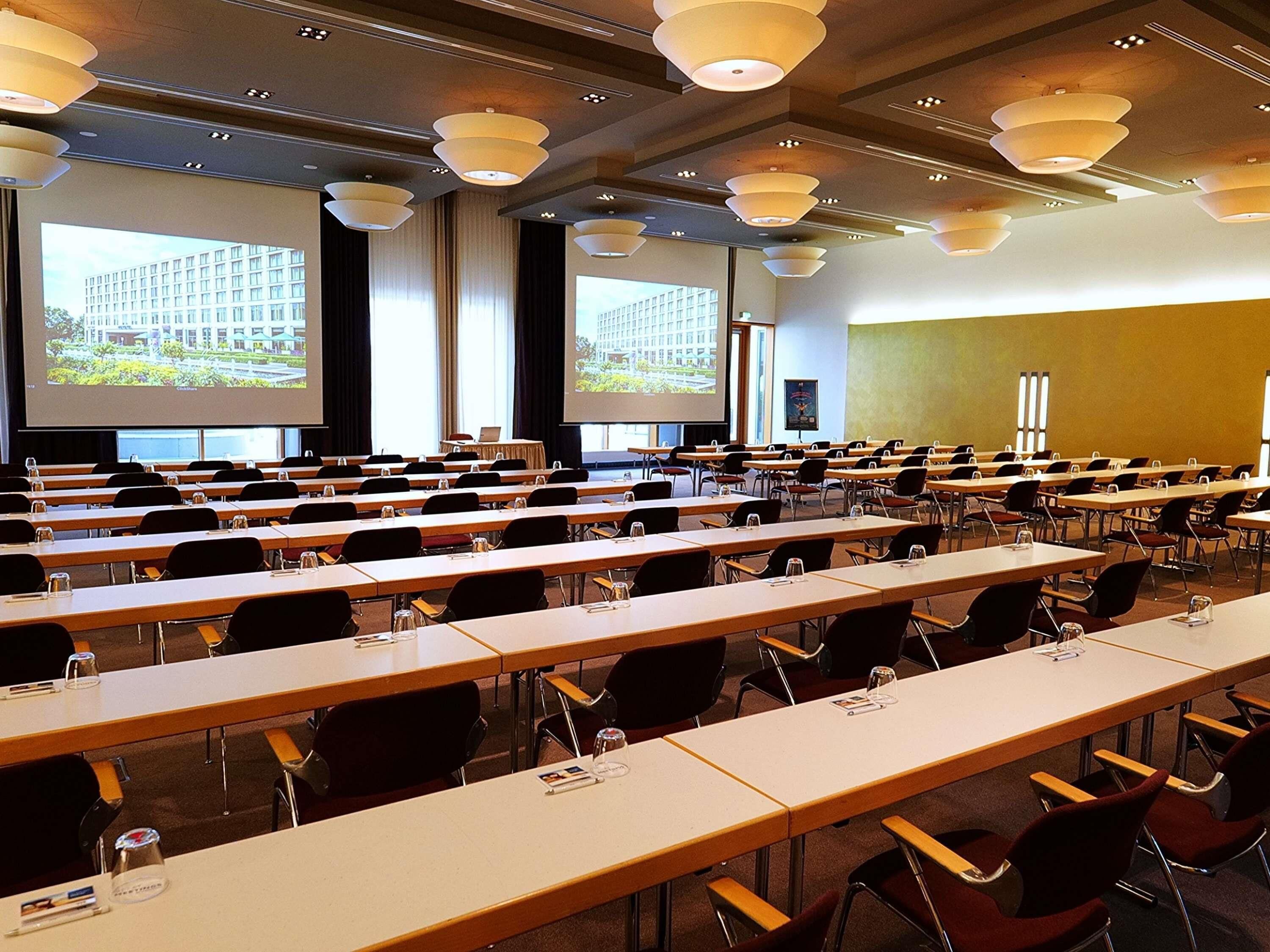 Ein Konferenzraum mit Tischen und Stühlen, einer großen Leinwand und einem Projektor.