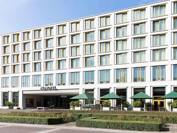 Un hotel moderno con fachada simétrica, numerosas ventanas y terraza exterior con sombrillas.