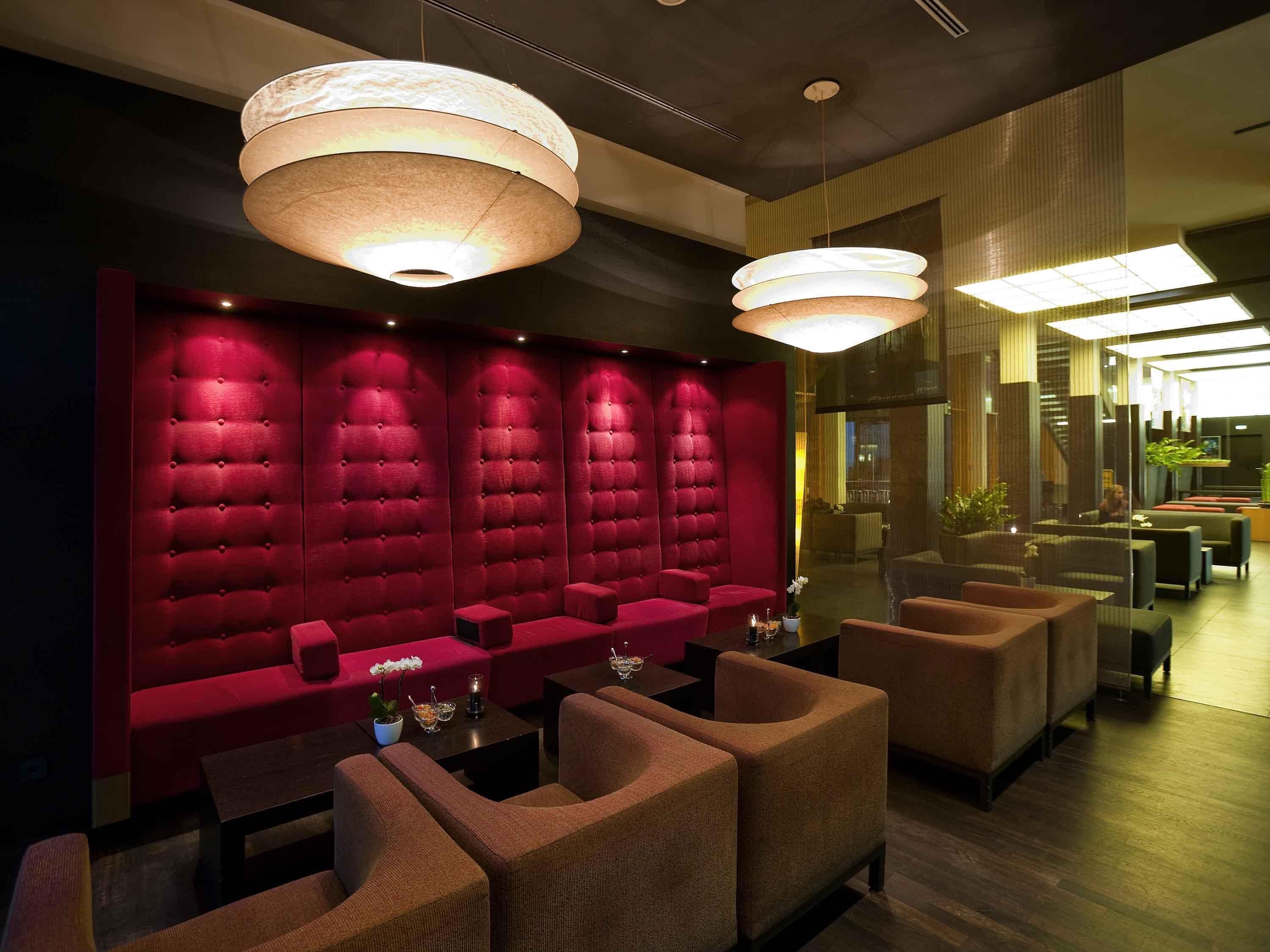 A modern lounge area with tufted red walls, comfortable seating, and pendant lighting.