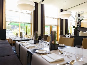A restaurant with tables set for dining, large windows, and indoor plants. - Novotel Karlsruhe City (Karlsruhe)