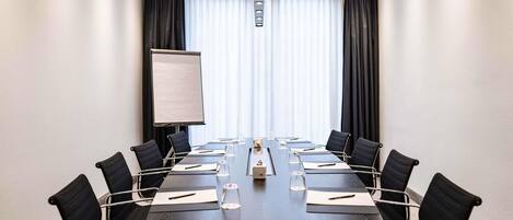 Un salón de conferencias con una larga mesa, sillas negras, una pizarra y vistas al exterior a través de amplios ventanales.