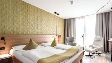 A hotel room with a large bed, a desk, a chair, and a window with curtains.