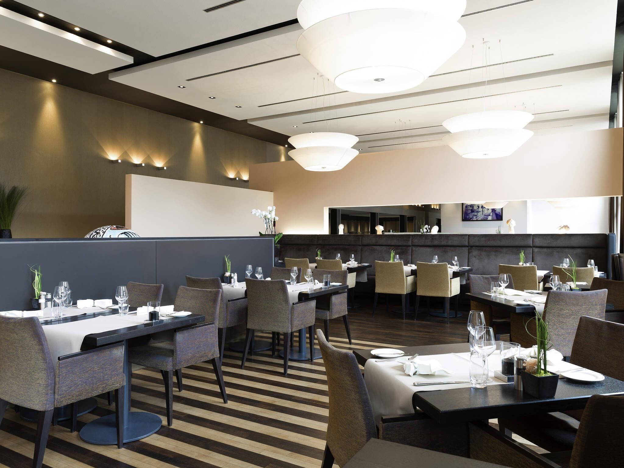 Un restaurant moderne doté d’un bar central, de nombreuses tables et d’un éclairage contemporain.