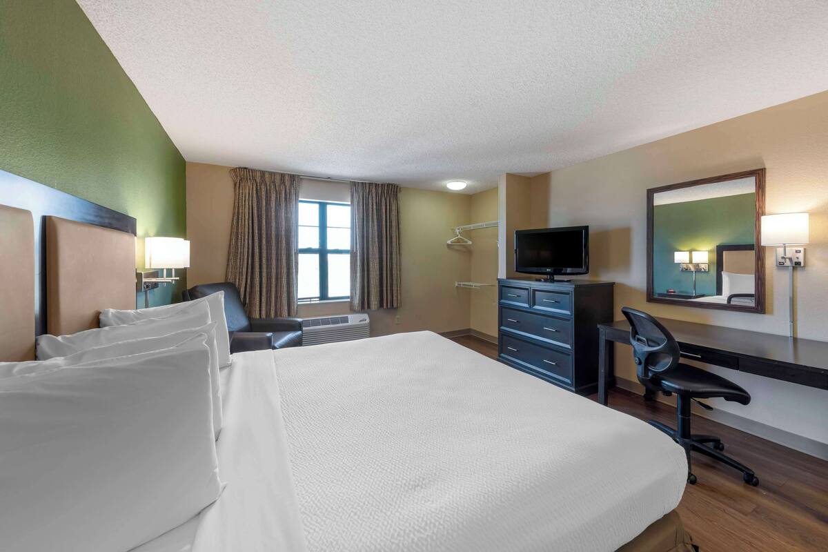 A hotel room with a large bed, a desk with a chair, a television, and a mirror on the wall.