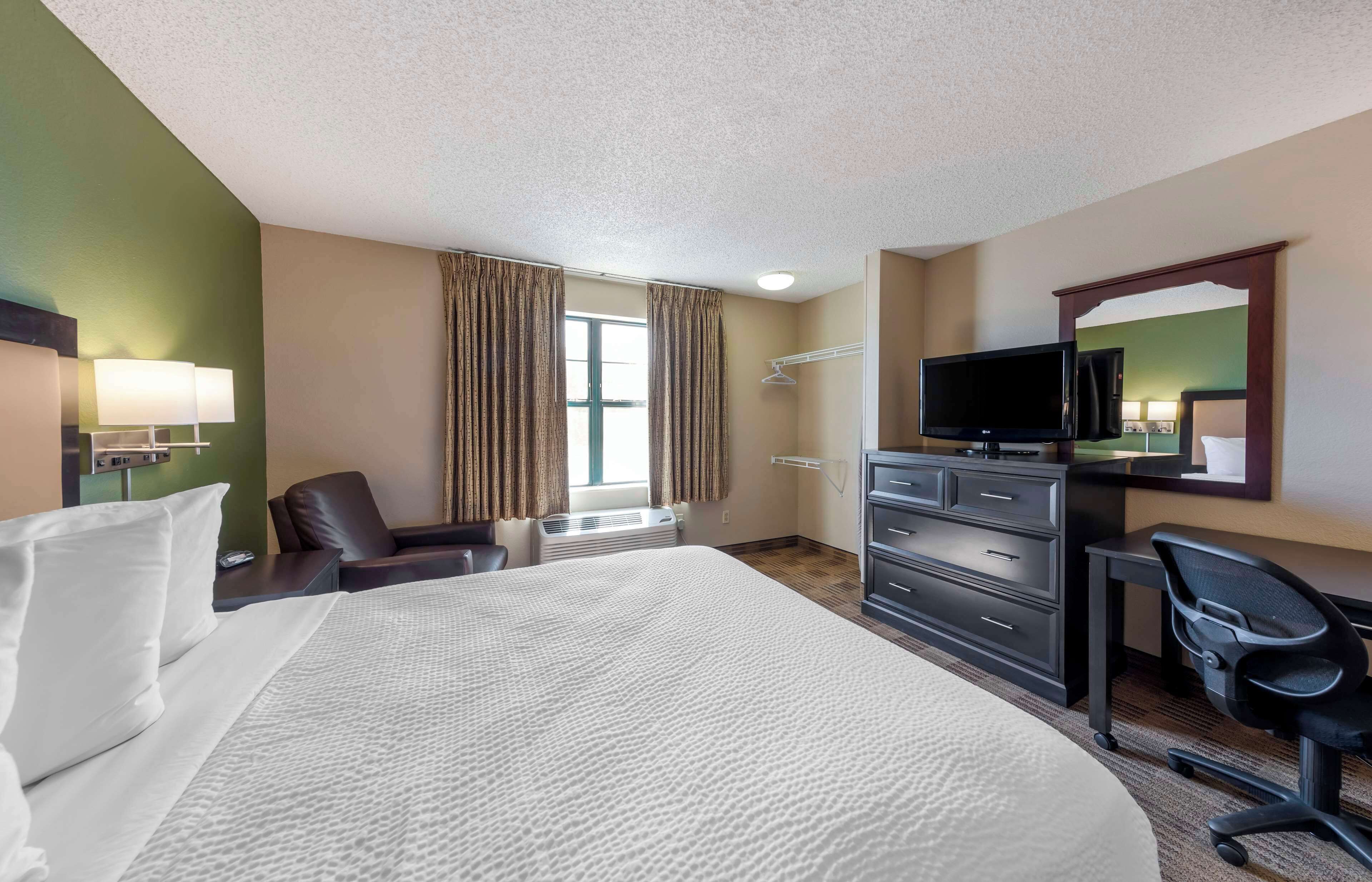 A hotel room with a large bed, a desk with a chair, a television, and a wardrobe.