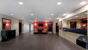 Un hall de hotel con una recepción, un televisor montado en la pared y una zona de estar con dos sillones.