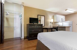 Quarto de hotel com cama, escrivaninha, televisão, armário, chuveiro e micro-ondas.
