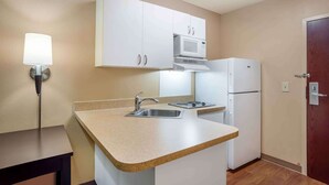 A compact kitchen with white cabinets, a microwave, a refrigerator, a sink, and a countertop.
