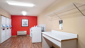 A laundry room with dryers, a white counter, and a red wall.