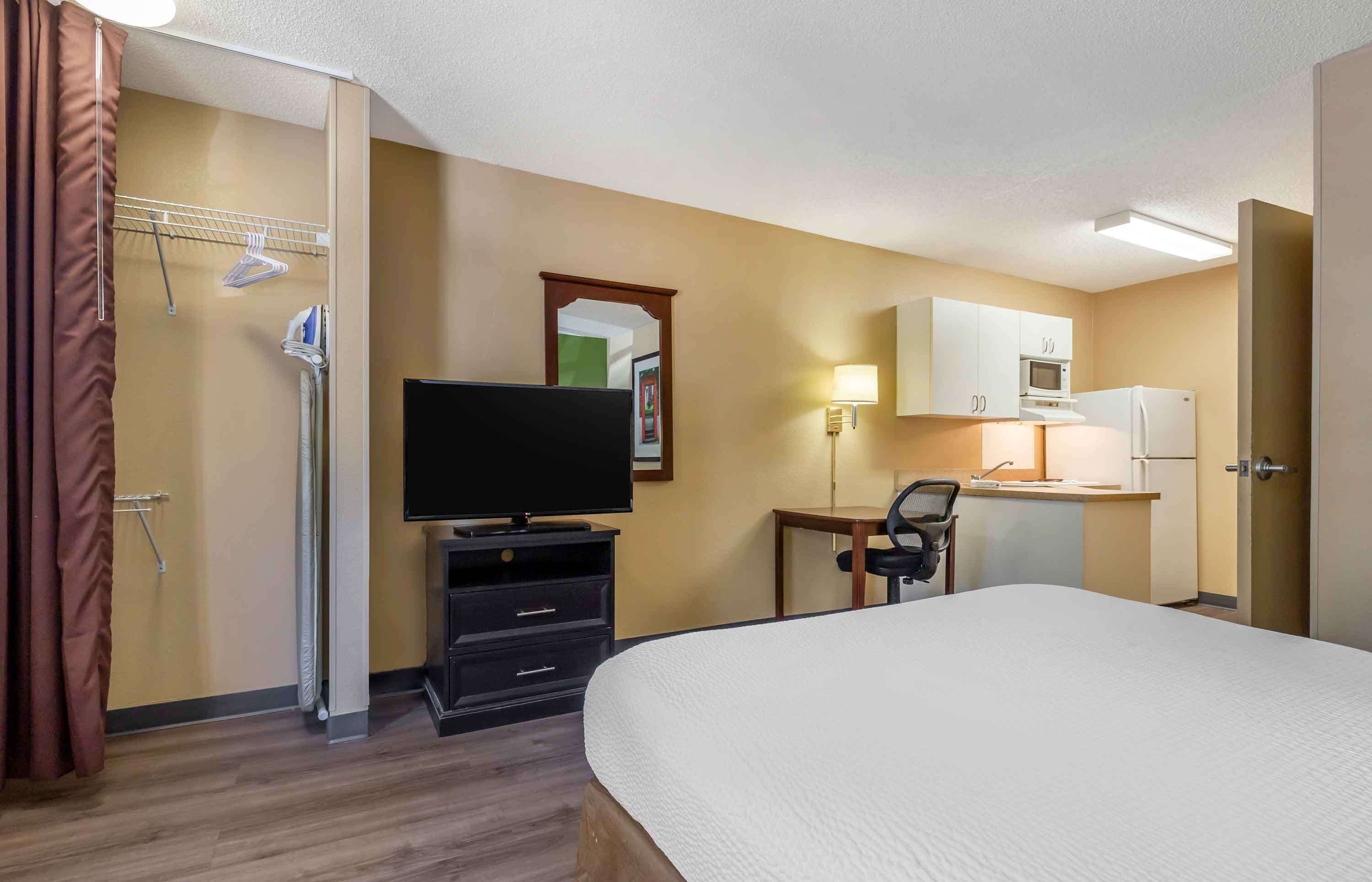 A hotel room with a bed, a television, a desk with a chair, a microwave, a refrigerator, and a small kitchenette.