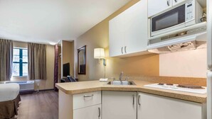 Une chambre d’hôtel compacte comprenant un coin cuisine, un lit, une fenêtre avec des rideaux et une lampe fixée au mur.