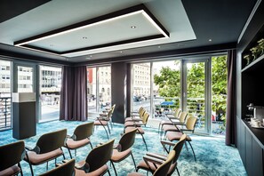 A conference room with rows of chairs, large windows with a city view, and a blue carpet.