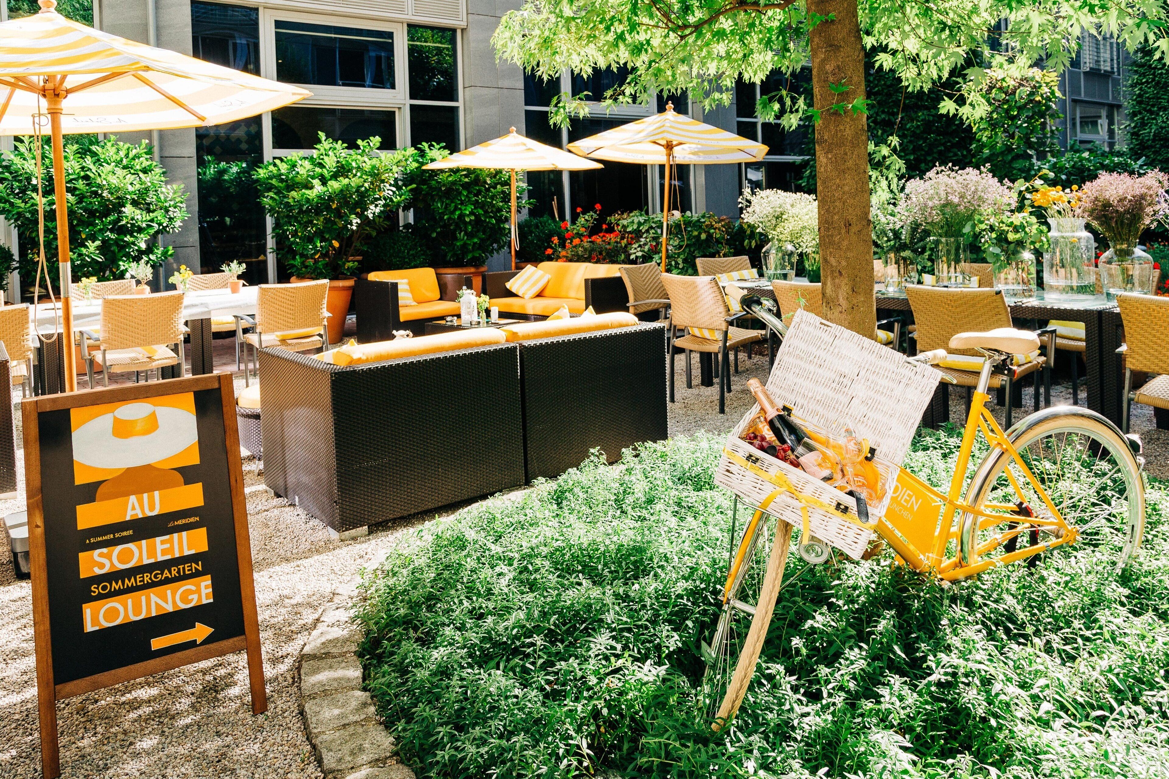 An outdoor seating area with wicker furniture, yellow cushions, and umbrellas. A sign points to the lounge area.