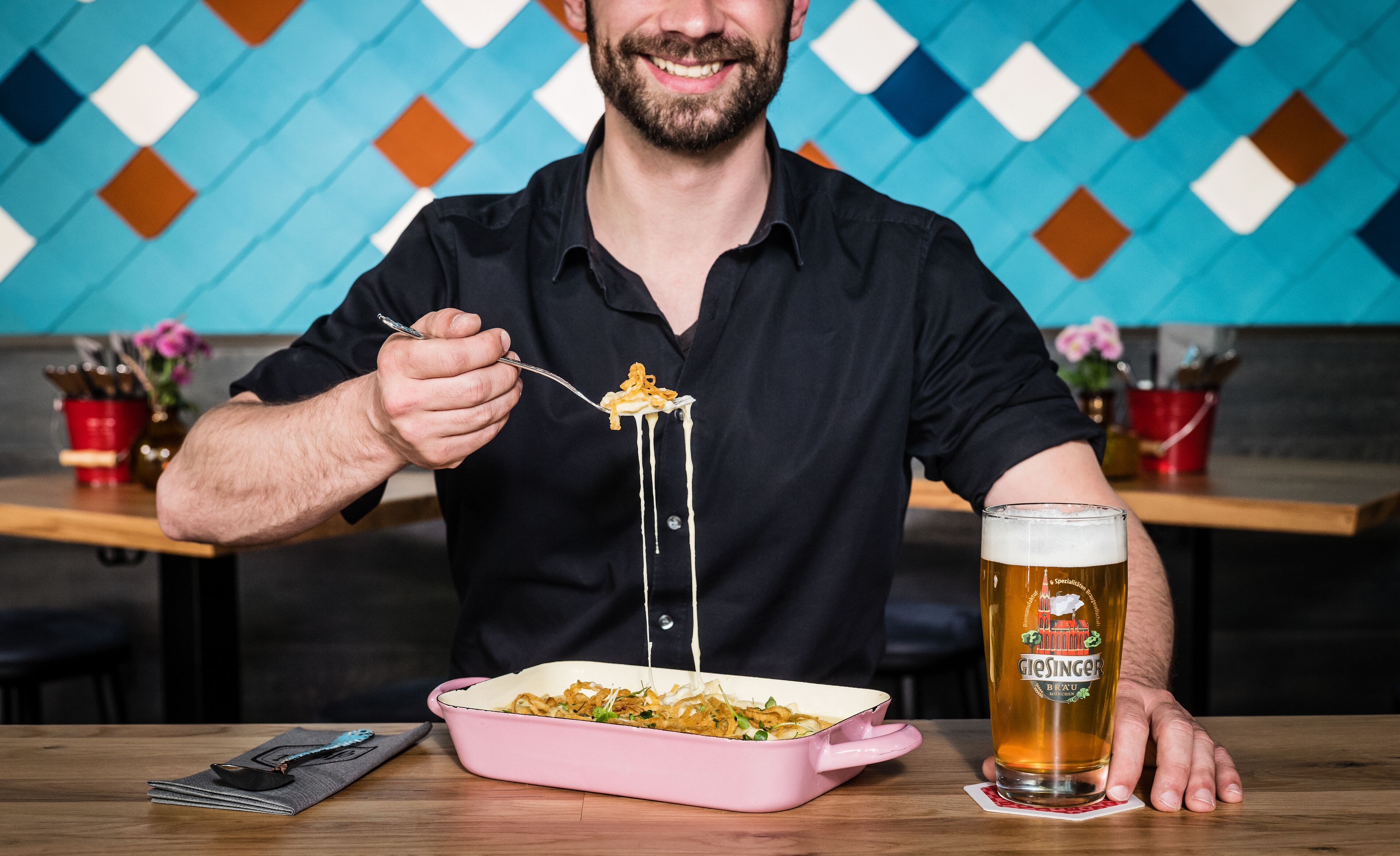 Eine Person isst an einem Tisch, neben einem rosa Auflauf und einem Glas Bier.