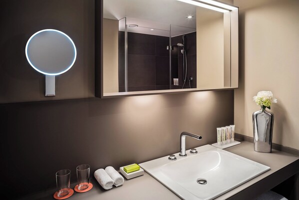 A modern bathroom with a large mirror, a round mirror, a sink, and a shower.