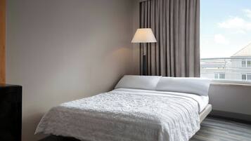 A hotel room with a bed, a lamp, and a view of buildings through the window.