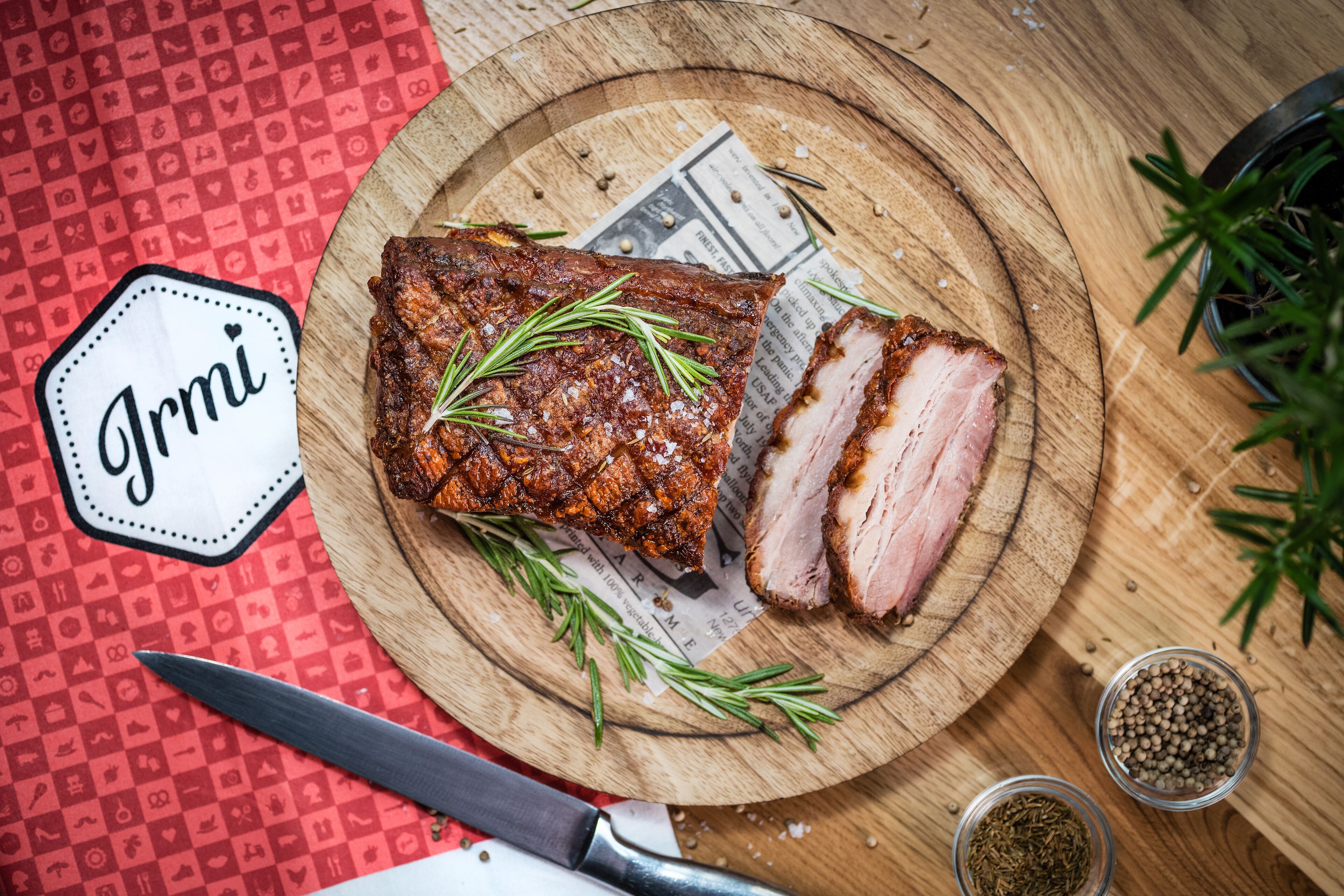 A wooden cutting board with sliced meat, rosemary, and peppercorns.