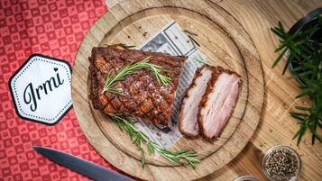A wooden cutting board with sliced meat, rosemary, and peppercorns.