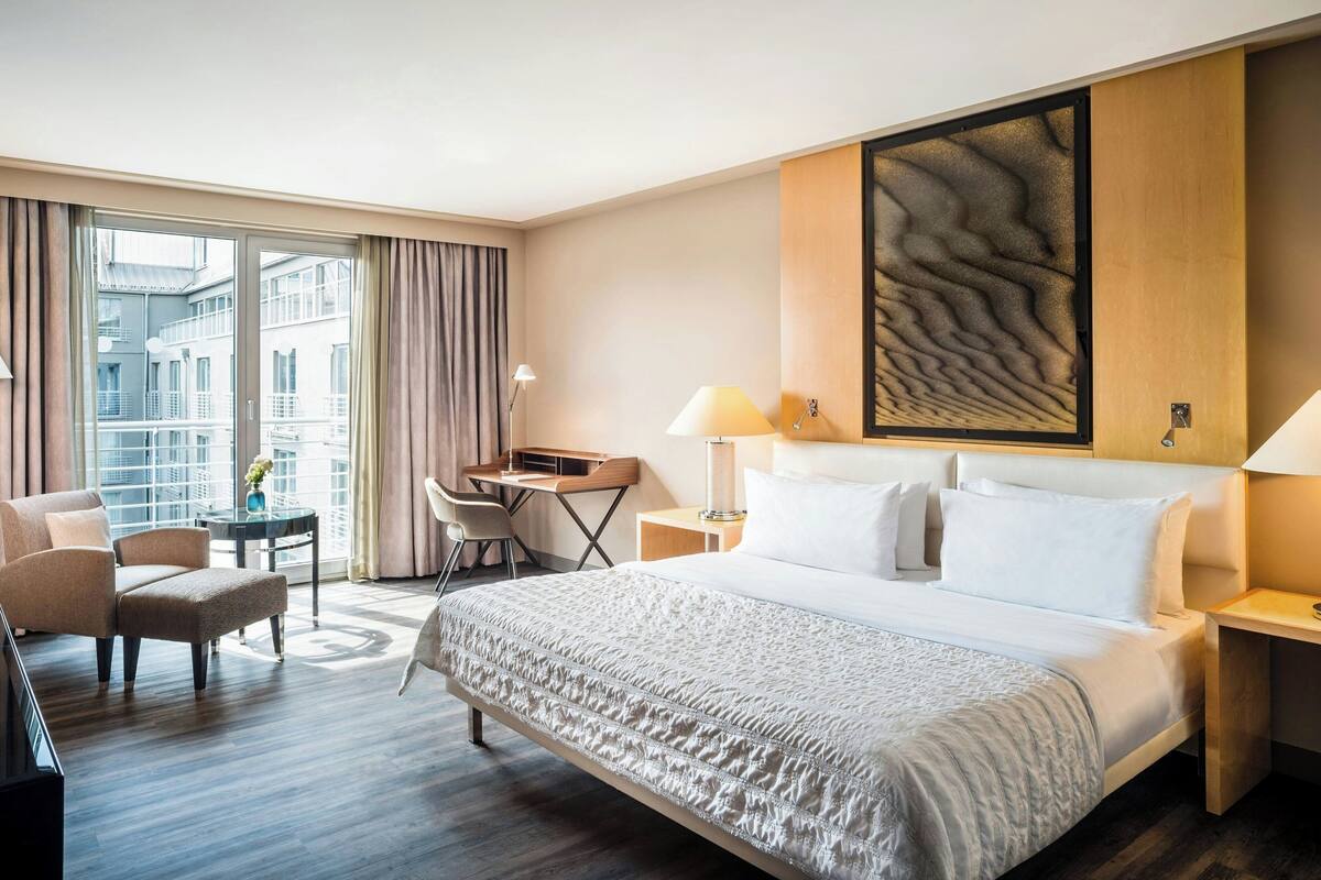 Hotellihuone, jossa on suuri sänky, työpöytä, tuoli ja ikkunasta avautuva näkymä kaupunkiin.
