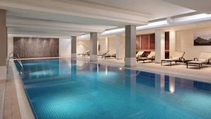 A large indoor swimming pool with lounge chairs and a modern ceiling design.