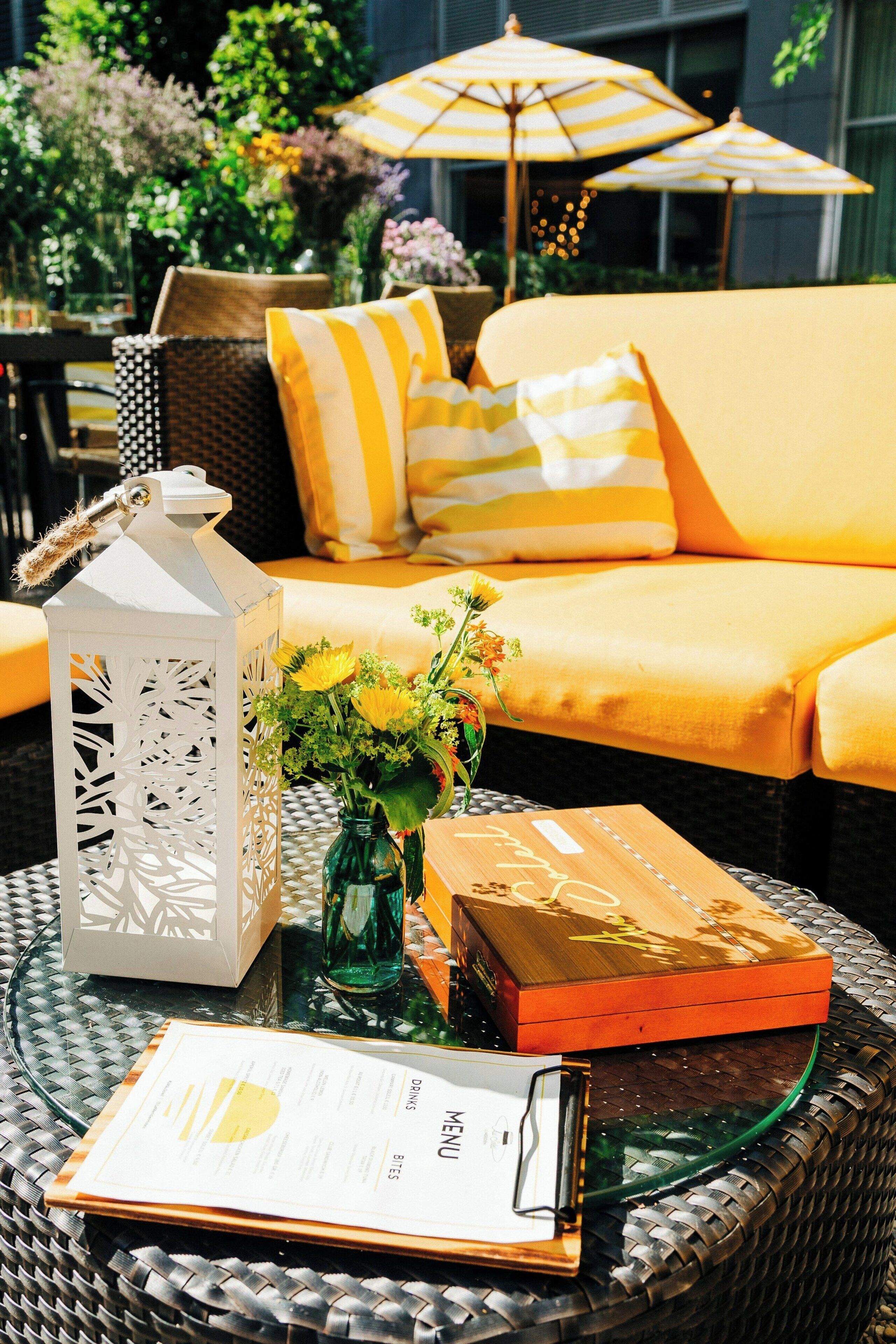 A dining area with a wicker table, a menu, a lantern, and a vase of flowers.