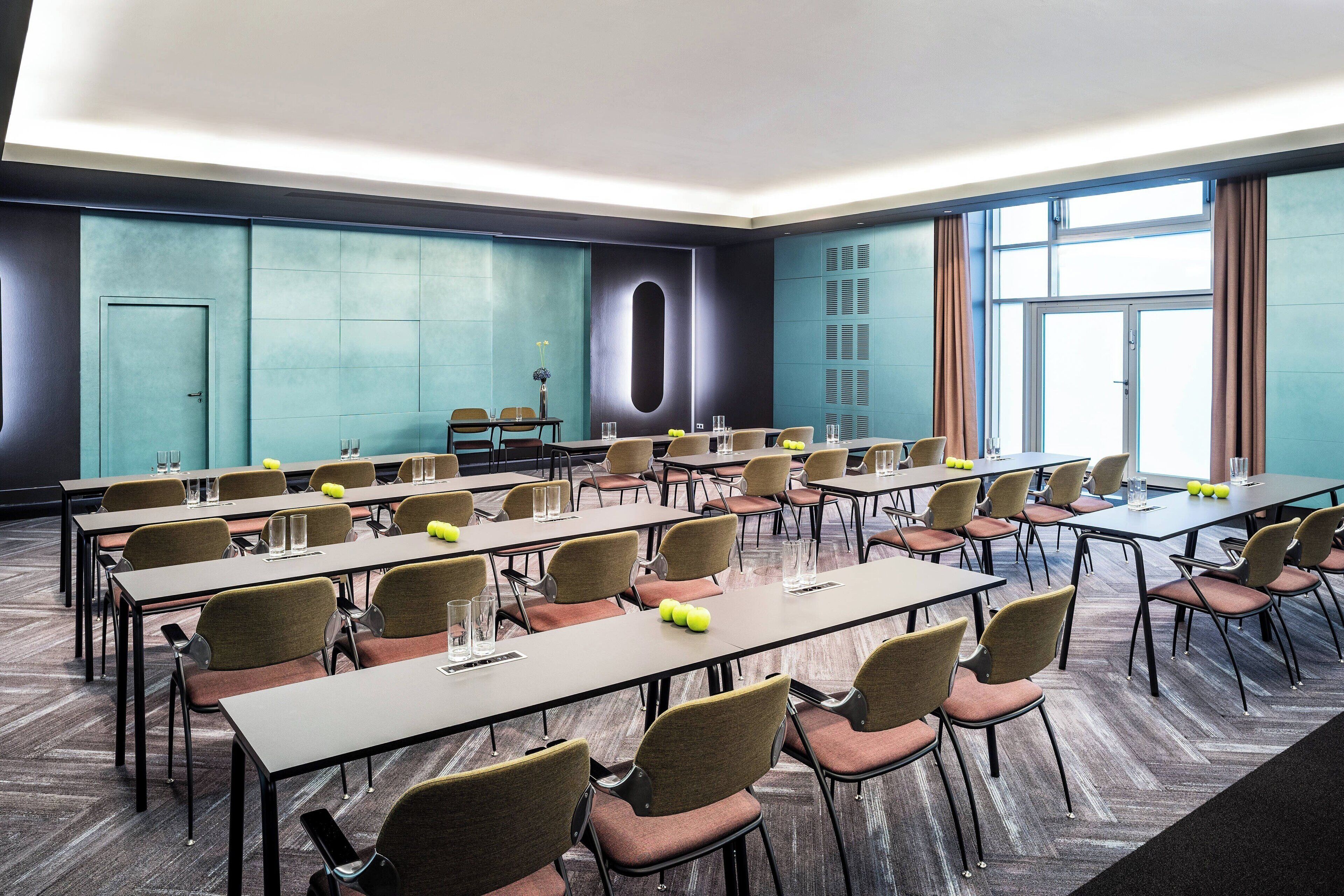 Un salón de conferencias con varias mesas y sillas, un ventanal grande y una puerta.