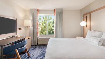A hotel room with a bed, desk, chair, TV, lamp, and window with curtains.