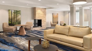 Eine moderne Hotelhalle mit beiger Couch, runden Tischen und einer Wand aus Stein.