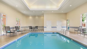 Ein Swimmingpool mit Liegestühlen und Tischen, ein Fliesenboden und eine Decke mit Einbaustrahlern.