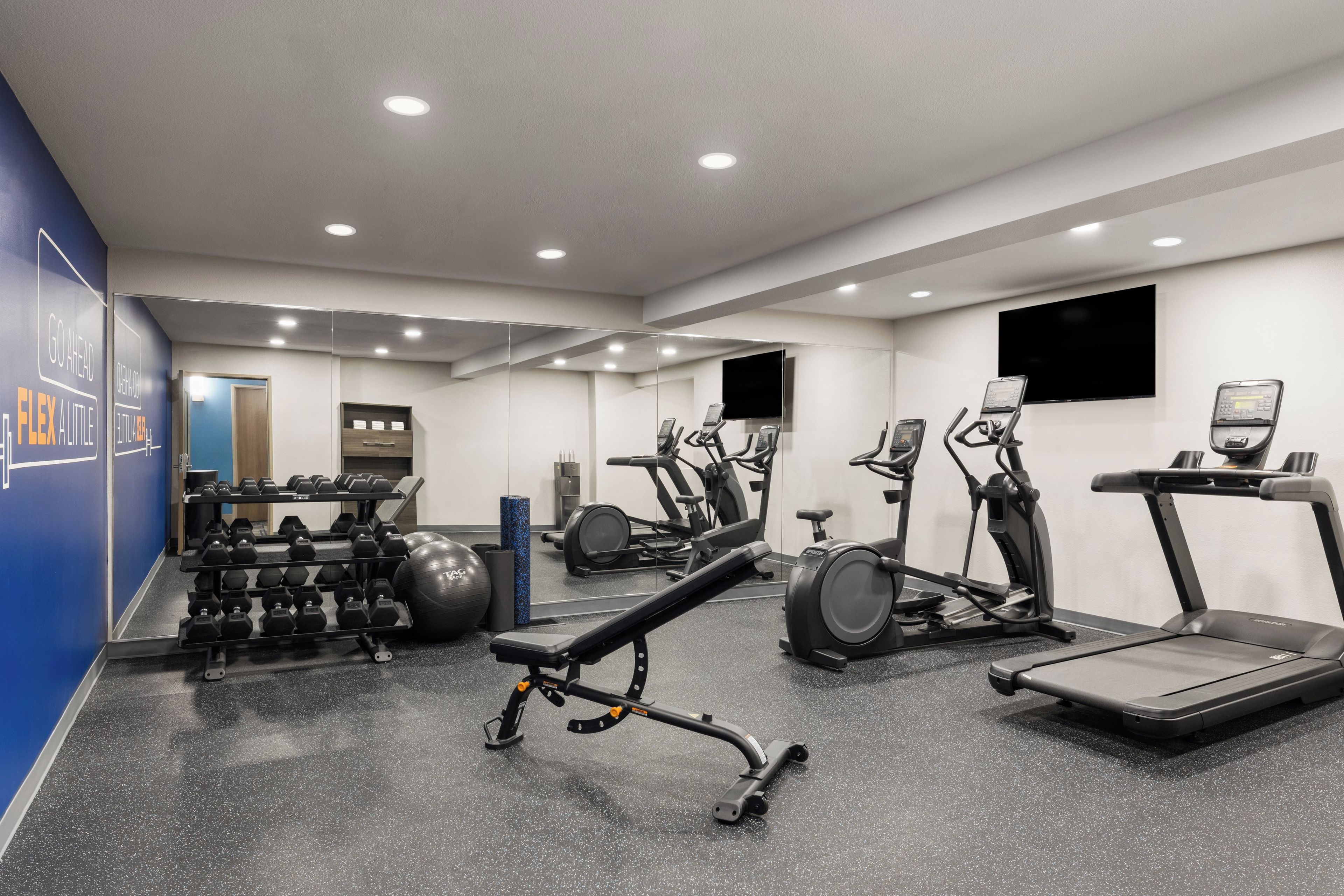 Une salle de sport équipée de divers appareils d’exercice, notamment des tapis de course, des appareils elliptiques et des poids libres.