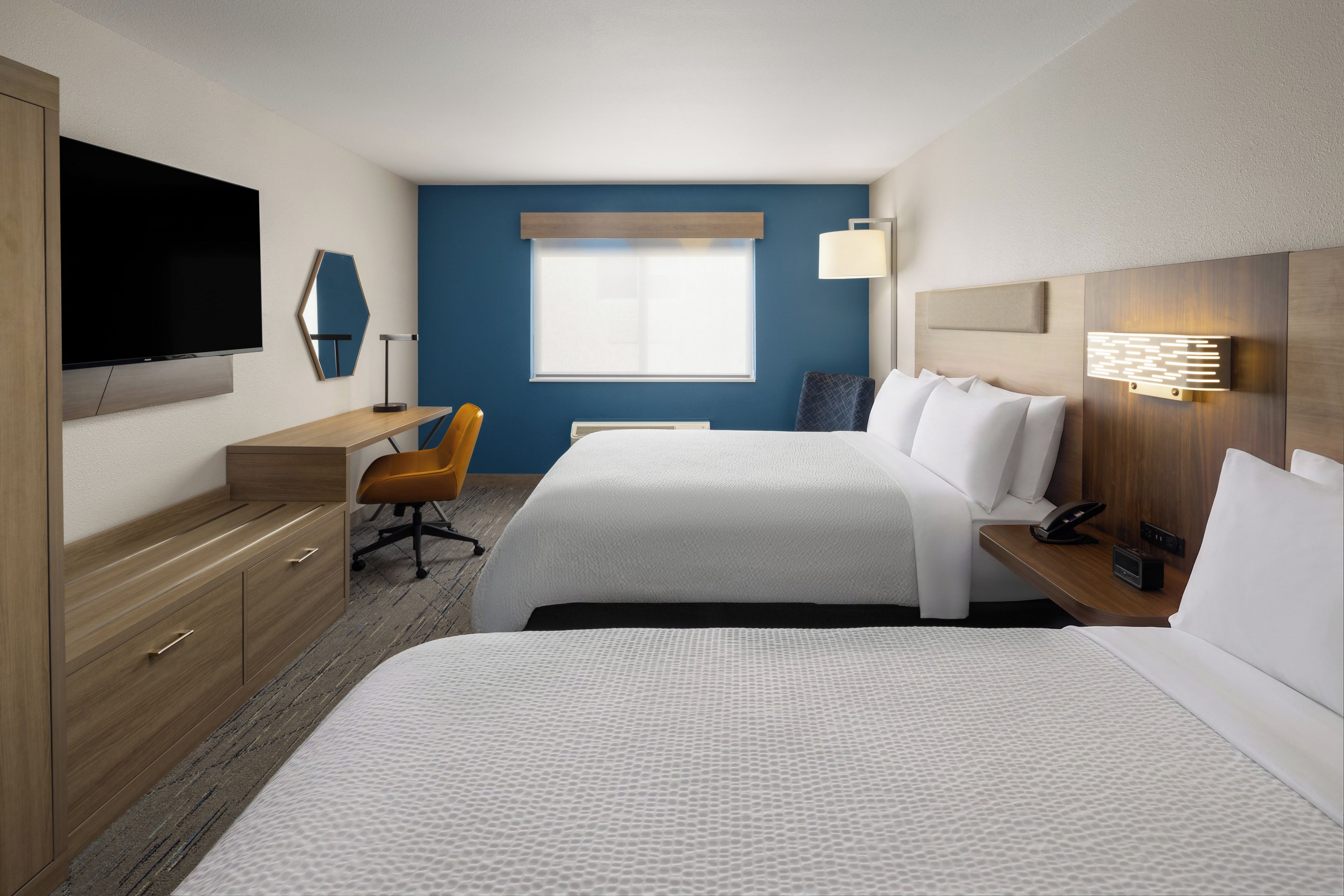 A hotel room with two beds, a desk, a chair, a television, and a window.