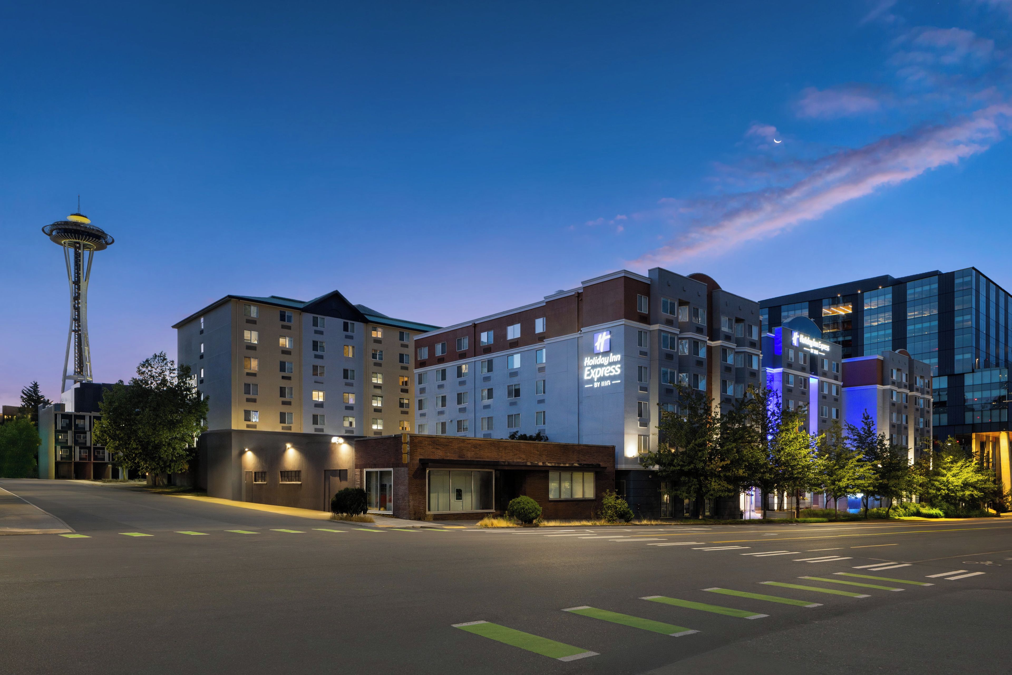 Un hotel de varios pisos con un letrero de Holiday Inn Express, una torre destacada al fondo y un cielo despejado.