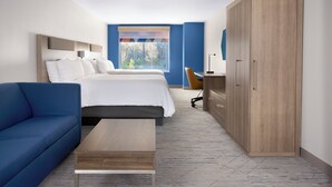 Quarto de hotel com cama, sofá azul, escrivaninha e guarda-roupa.
