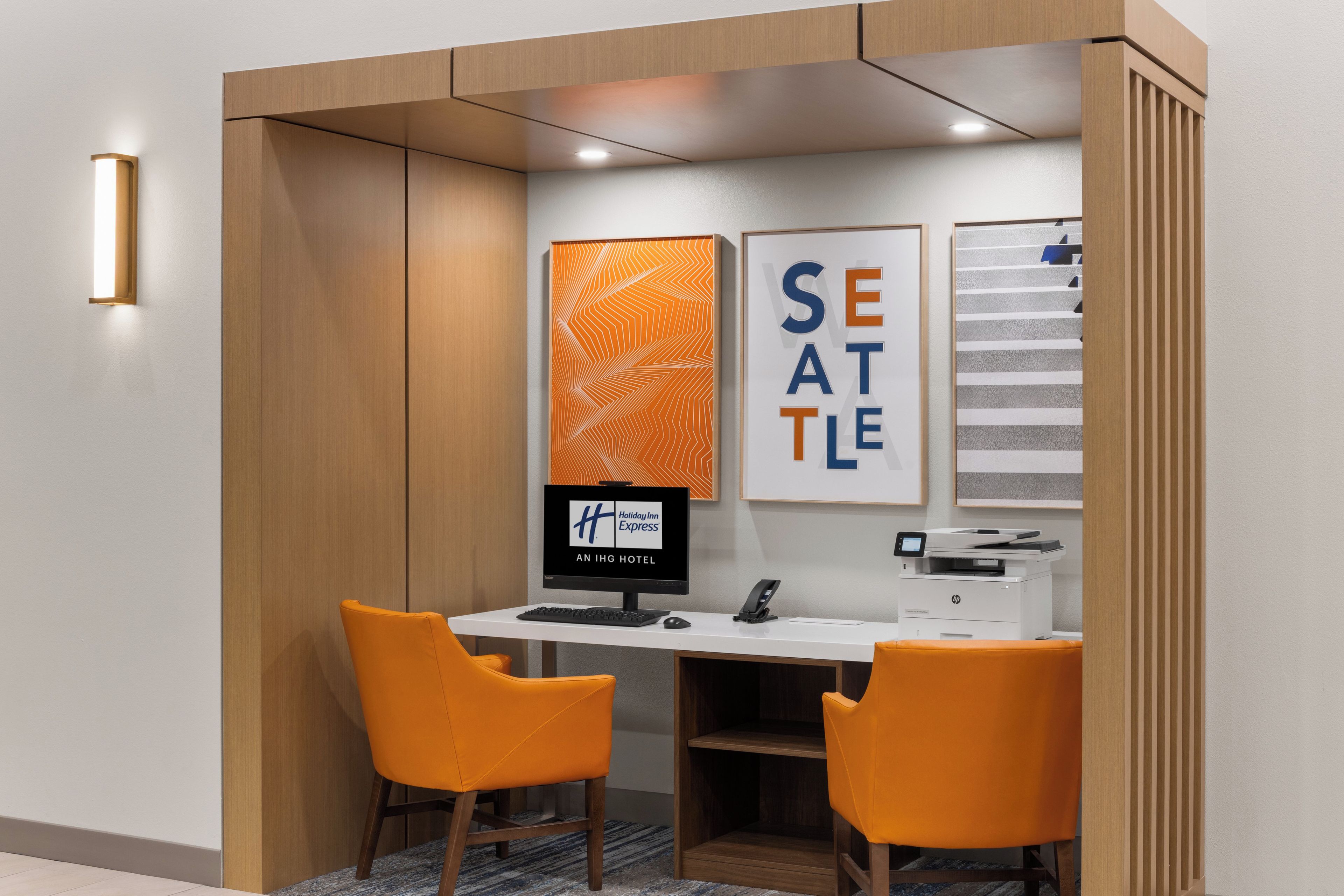 A hotel room with a desk, two orange chairs, a computer, and a printer.