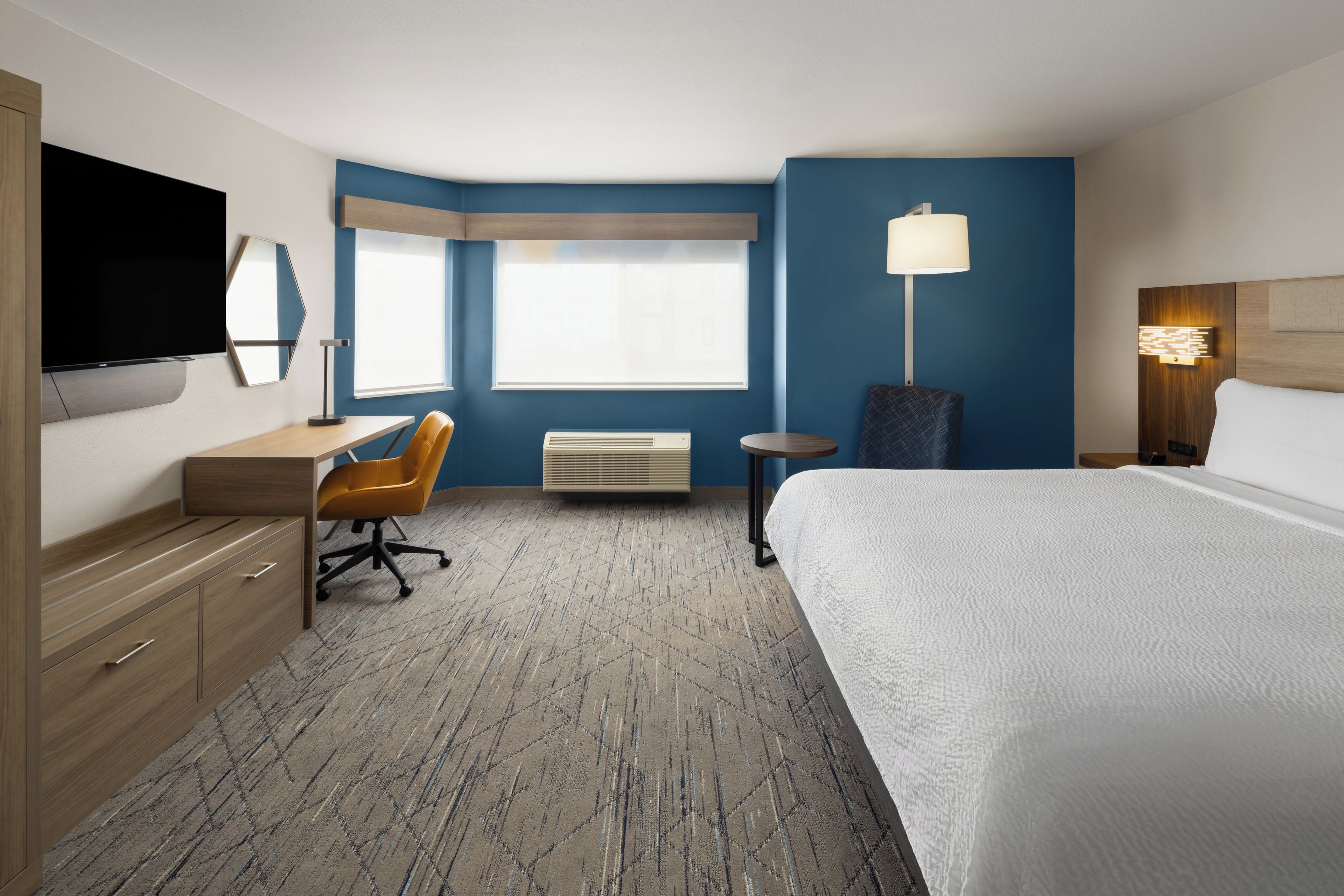 A hotel room with a bed, desk, chair, television, and a window.