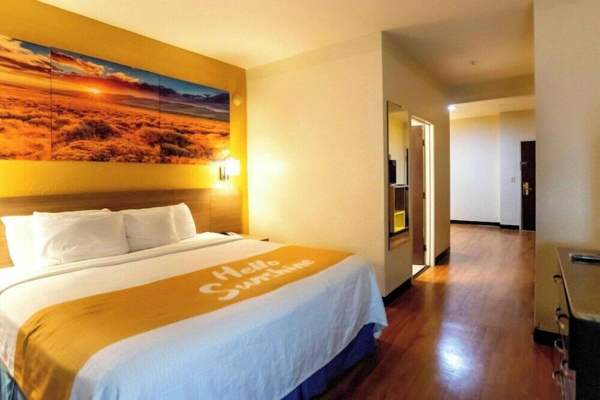 Ein Hotelzimmer mit einem Bett, einem Bild an der Wand und einem Flur zu weiteren Zimmern.