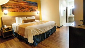 A hotel room with a large bed, a nightstand, a desk, and a painting on the wall. - Days Inn & Suites by Wyndham Houston North/Aldine (Houston)