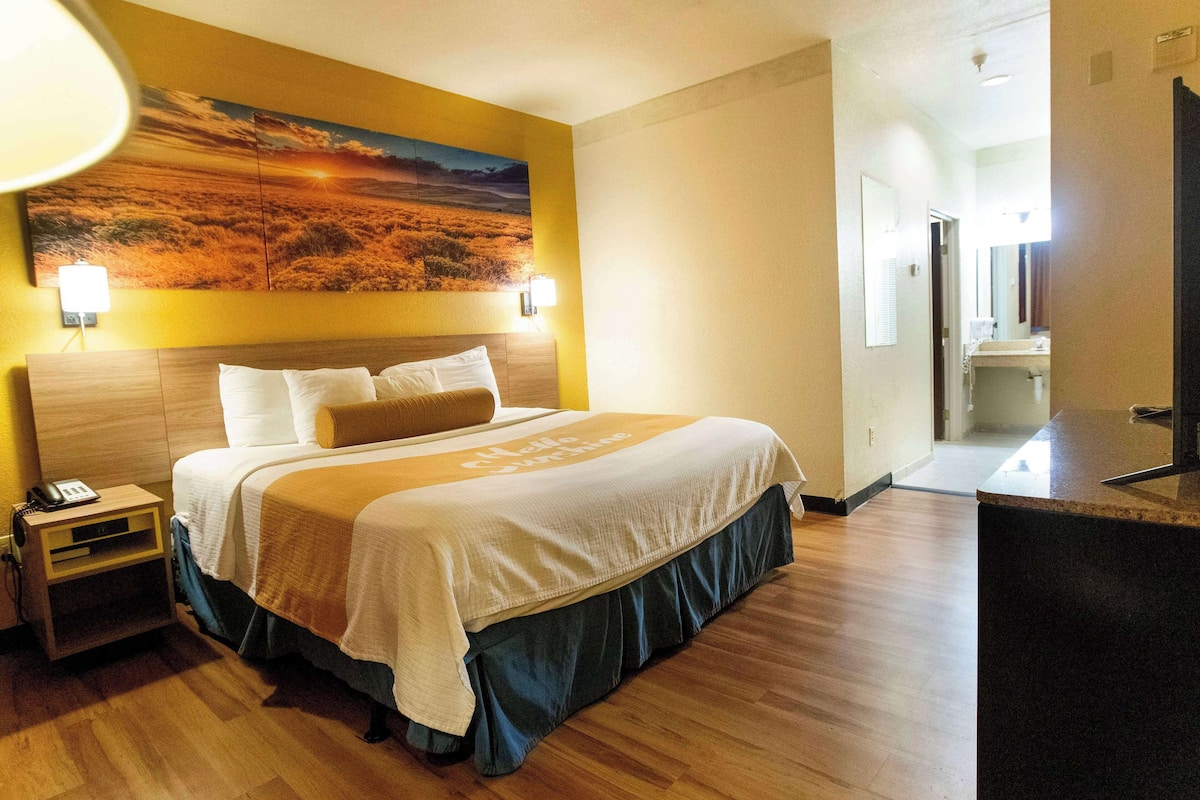 Ein Hotelzimmer mit einem großen Bett, einem Nachttisch, einem Schreibtisch und einem Gemälde an der Wand.